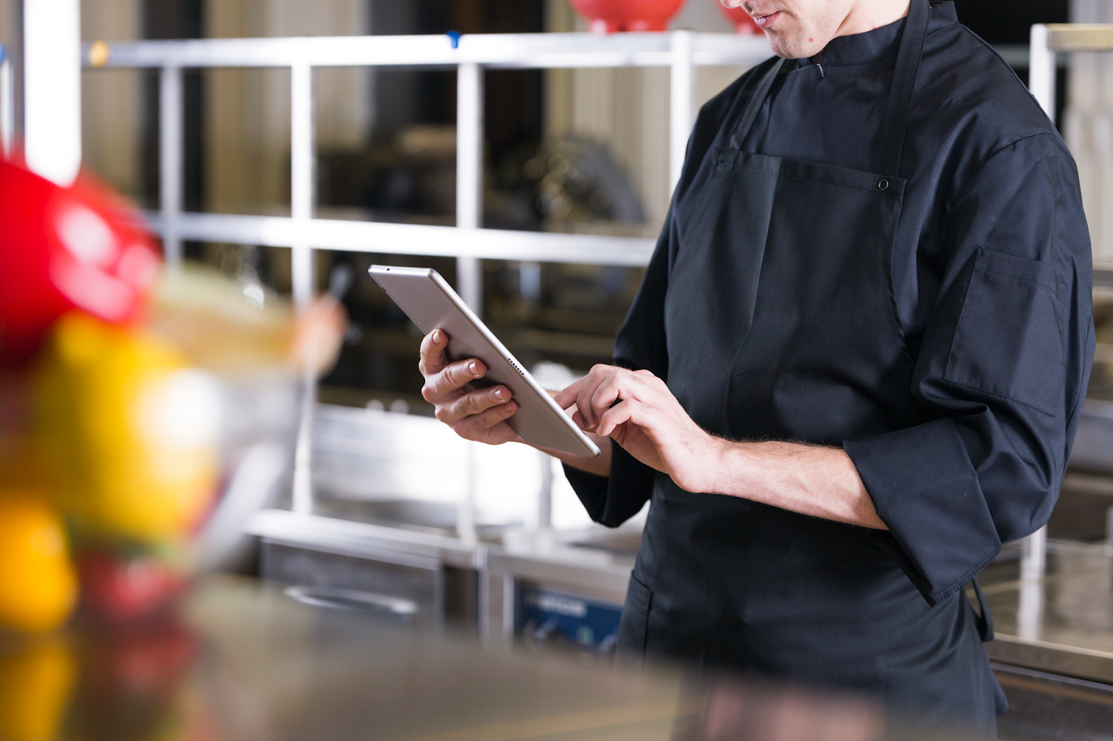 Chef in black uniform using a tablet in a commercial kitchen setting.